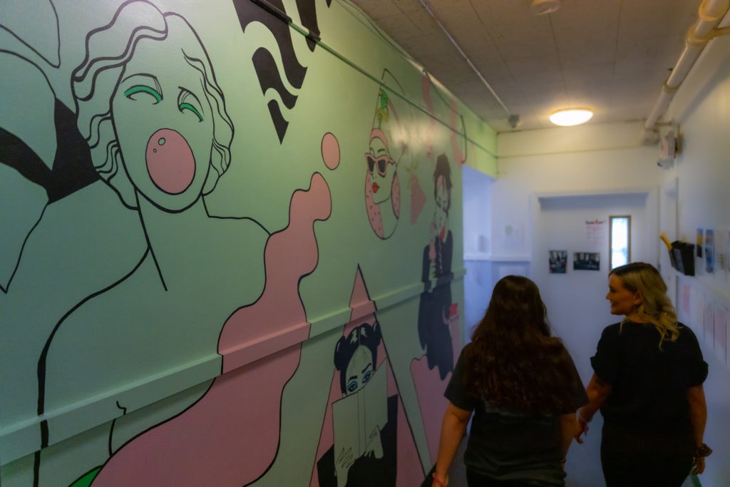 Two people walk down a hall alongside a mural at The Chase Home